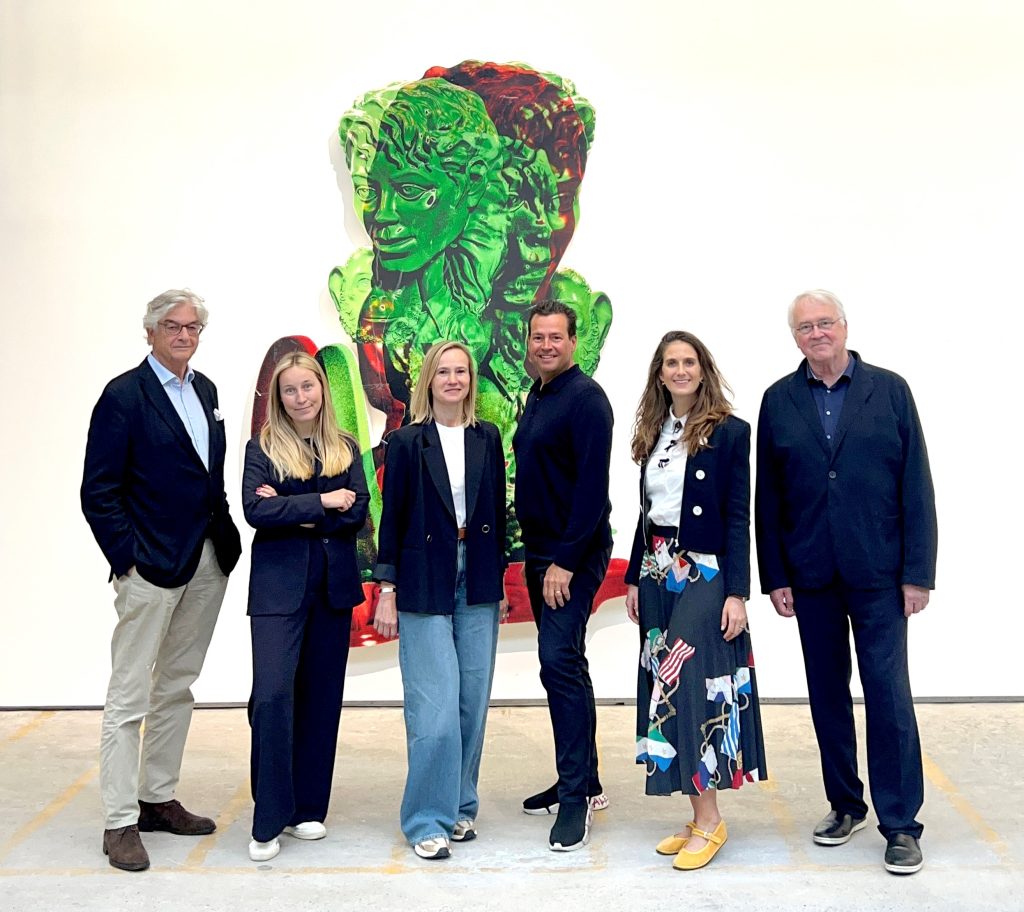Group of six Caucasian adults, three women, three men, posing together in front of a piece of figurative, green abstracted contemporary art in a gallery setting. 